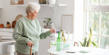 Mutfaktaki masada cam çöp kutusuna sopa yerleştiren son sınıf öğrencisi bir kadın.