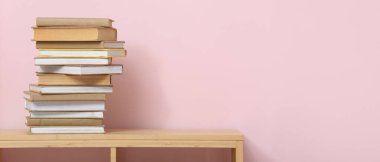 Renk duvarının yanındaki ahşap raf ünitesinde yığınla farklı kitap var.