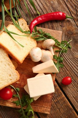 Kahverengi ahşap arka planda işlenmiş peynir, ekmek ve sebzeli tahta.
