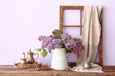 Vazoda leylak demeti ve duvarın yanındaki ahşap masada mutfak gereçleri.