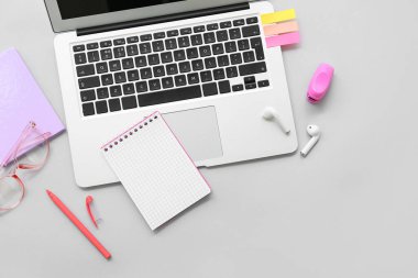 Gözlüklü, kulaklıklı ve gri arka planda kırtasiyeli dizüstü bilgisayar.