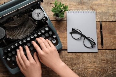 Kahverengi ahşap arka planda daktilo, gözlük, defter ve çiçekle daktilo kullanan kadın.