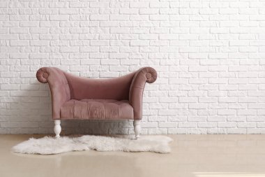 Beyaz tuğla duvarın yanında rahat pembe koltuk ve kürk halı.