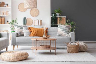 Gri kanepe, sehpa ve hasır puflarla aydınlık oturma odasının içinde.