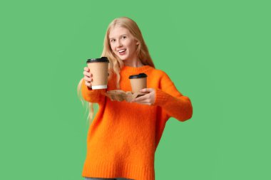 Yeşil arka planda çay fincanları olan güzel, genç ve mutlu bir kadın.