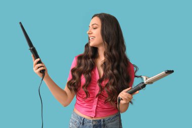 Mavi arka planda farklı saç maşaları olan güzel genç bir kadın.