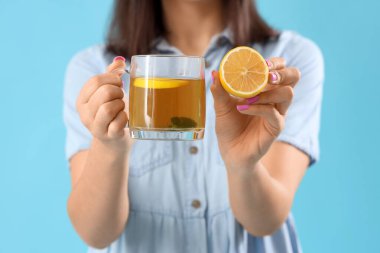 Mavi arka planda cam bardak çay ve limonlu genç bayan, yakın plan.