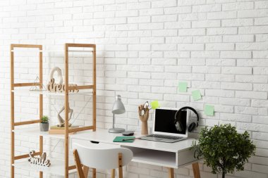 Beyaz duvarın yanında işyeri, ev bitkisi ve raf ünitesi olan modern bir oda.