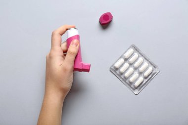 Astım spreyli bir çocuk eli ve beyaz arka planda haplar.