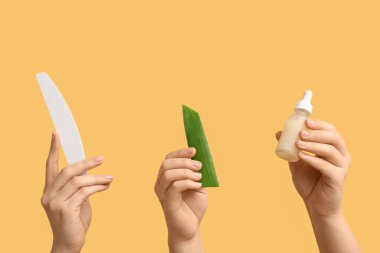 Tırnak törpüsü ve sarı arka planda aloe vera ile tırnak yağı şişesi tutan kadın eller.