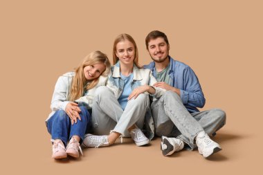 Kahverengi arka planda oturan şık kot elbiseli mutlu bir aile.