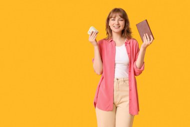 Sarı arka planda cüzdan ve para tutan güzel genç bir kadın.