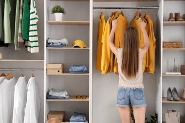 Soyunma odasında şık kıyafetler düzenleyen güzel genç bir kadın.