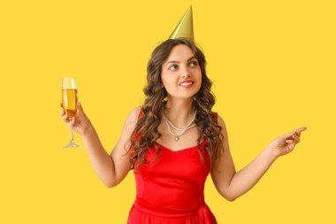 Doğum günü şapkalı genç bir kadın ve sarı arka planda bir bardak şampanyayla
