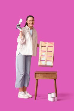 Çalı çırpı kaplı genç bir kadın mor arka planda ahşap kutu boyuyor