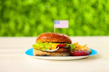 Amerikan bayrağıyla lezzetli bir burger ve açık havada patates kızartması, yakın plan. Amerikan Bağımsızlık Günü kutlamaları