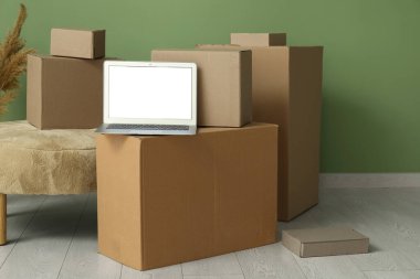 Boş dizüstü bilgisayar, taşınan kutular ve yeşil duvarın yanında pouf.