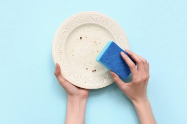 Eller mavi arka planda bulaşıkları yıkıyor.