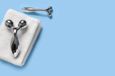 Mavi arka planda yüz masajı aletleri ve havlu.