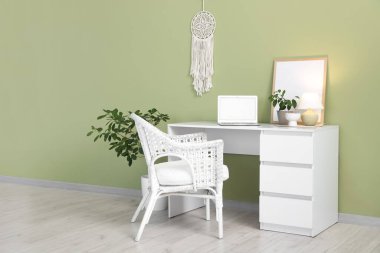 Laptop, ev bitkisi ve yeşil duvarın yanında parlayan masa lambasıyla modern çalışma alanı