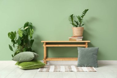 Yeşil duvarın yanında çiçekli ve yastıklı bir bank.