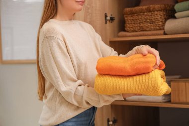 Dolaptaki raflara şık giysiler koyan genç bir kadın.