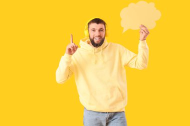 Sarı arka planda boş konuşma balonu olan kulaklıklı yakışıklı genç adam.