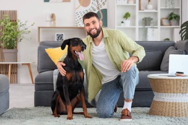 Genç adam evde Dobermann 'ın köpeğine sarılıyor.