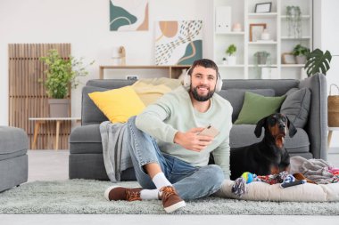 Kulaklıklı genç adam ve evde Dobermann köpeği var.