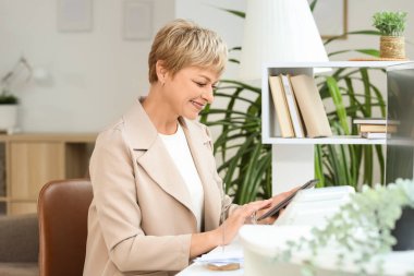 Ofiste tablet bilgisayarla çalışan olgun bir iş kadını.