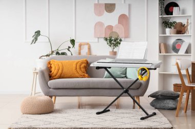 Aydınlık oturma odasının içinde sentezleyici, koltuk ve raf ünitesi var.