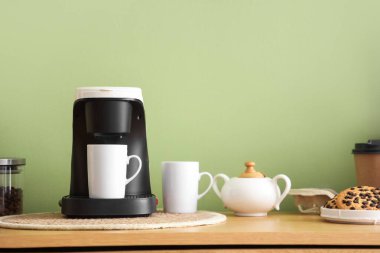 Yeşil duvarın yanındaki klozette fincanlı, şekerli ve kurabiyeli kahve makinesi.