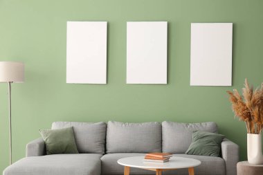 Rahat bir kanepe, masa ve yeşil duvarda boş posterler.
