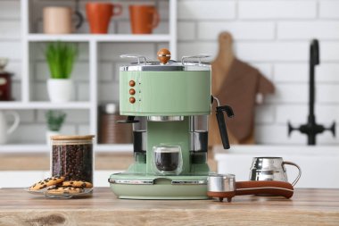 Modern kahve makinesi, bir bardak sıcak espresso ve mutfaktaki ahşap masada bir tabak tatlı kurabiye.