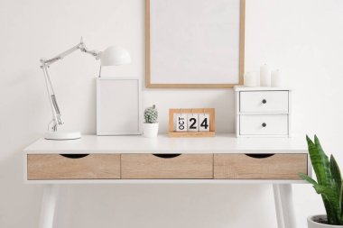 Masa lambası, takvimi ve beyaz duvarın yanında mumları olan modern masa.