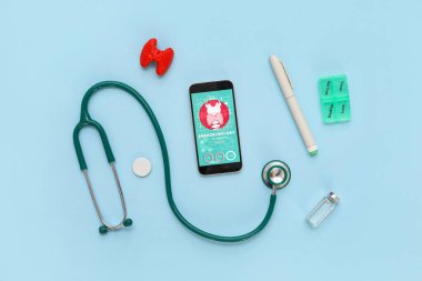 Tiroid bezi modelli cep telefonu, kareli kalem ve mavi arka planda steteskop. Endokrinoloji kavramı