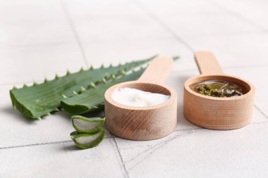 Ahşap kaşık kozmetik krem ve aloe vera yapraklı jöle beyaz fayans arka planda, yakın çekim