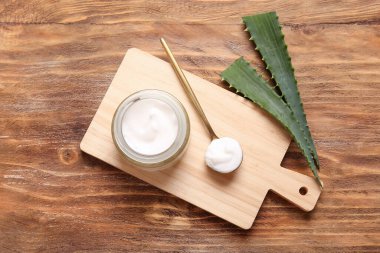 Ahşap arka planda aloe vera yapraklı kavanoz ve kaşık dolusu kozmetik krem.