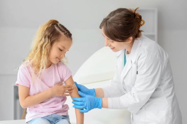 Klinikteki aşıdan sonra küçük kızın koluna bant yapıştıran kadın doktor.