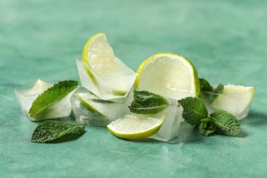 Buz küplerinde donmuş kireç dilimleri ve yeşil arka planda nane yaprakları.