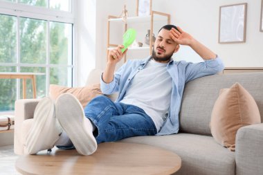 Küçük yelpazeli genç adam evdeki kanepede sıcaktan muzdarip.