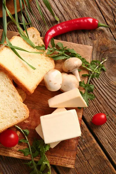 Kahverengi ahşap arka planda işlenmiş peynir, ekmek ve sebzeli tahta.