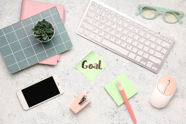 Kelime GOAL, kırtasiye, bilgisayar klavyesi, cep telefonu ve grunge arkaplanda gözlük içeren yapışkan bir not