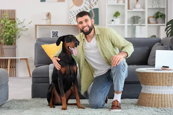 Genç adam evde Dobermann 'ın köpeğine sarılıyor.