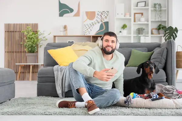 Kulaklıklı genç adam ve evde Dobermann köpeği var.