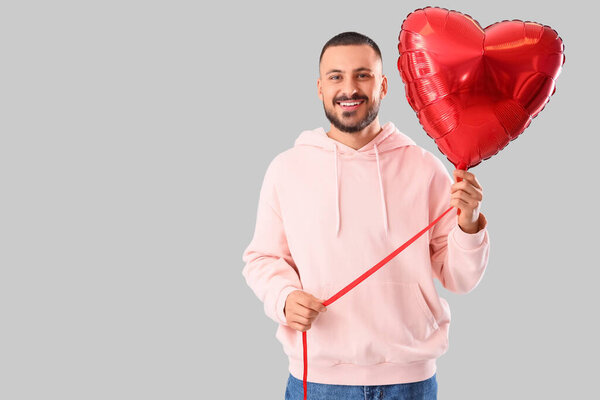 Красивый молодой счастливый человек с шаром в форме сердца на сером фоне