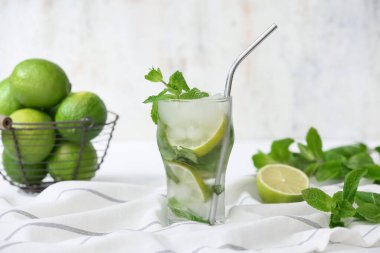 Bir bardak taze mojito kokteyli ve beyaz arka planda nane ve limon sepeti.