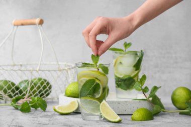 Taze Mojito kokteyli ve gri arka planda nane şekerli kadın eli.