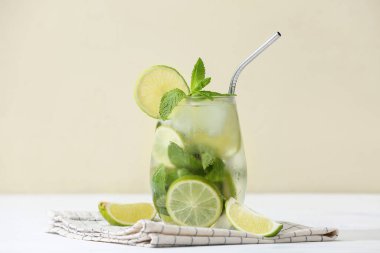 Bir bardak taze mojito kokteyli, beyaz masada limon ve nane.