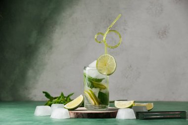 Bir bardak taze Mojito kokteyli ve yeşil masada buz küpleri.